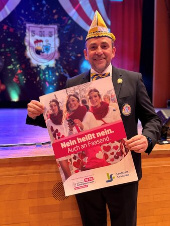 Michael Schleich Regionalvertreter des Verbandes saarländischer Karnevalsvereine im Bezirk Saarlouis/Lebach steht auf einer Bühne und hält ein Plakat mit der Aufschrift „Nein heißt nein. Auch an Faasend.“ 