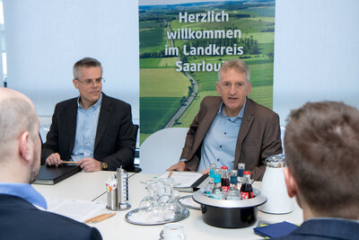 Mehrere Personen sitzen an einem Konferenztisch im Gespräch. Links der Oberbürgermeister der Kreisstadt Merzig, rechts der Landrat des Landkreises Saarlouis.