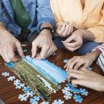 Drei Händepaare von einem Kind, einem Erwachsenen und einem Senior machen ein Puzzle.