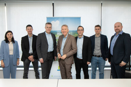 Sieben Personen stehen nebeneinander in einem Besprechungsraum und blicken in die Kamera.